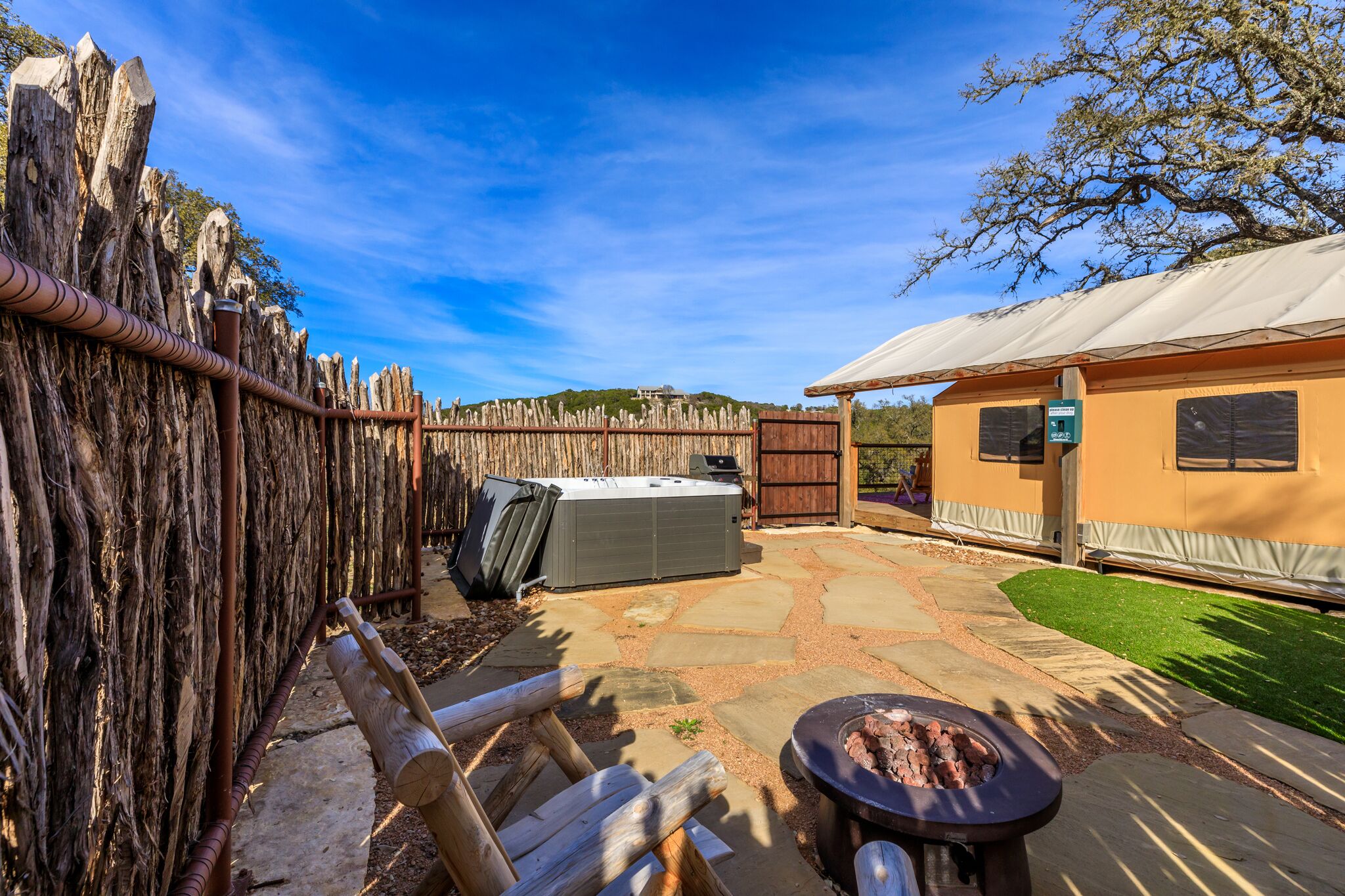 Un jardin avec une terrasse en pierre, un jacuzzi, un barbecue et une clôture en bois.