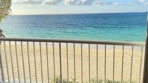Une vue sur la plage depuis un balcon doté d’une balustrade, avec un ciel dégagé et une mer calme.