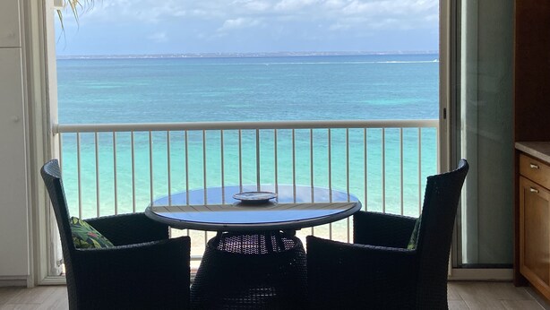 Un balcon avec une table et des chaises, donnant sur une mer turquoise et un ciel dégagé.
