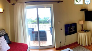 Une chambre avec un lit, une télévision, une table avec des télécommandes, une porte-fenêtre coulissante donnant sur une terrasse et une enseigne indiquant « Casa da Figueira ».