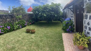 Un jardin bien entretenu, agrémenté d’un mur en pierre, d’un grand arbre et de plantes en pot.
