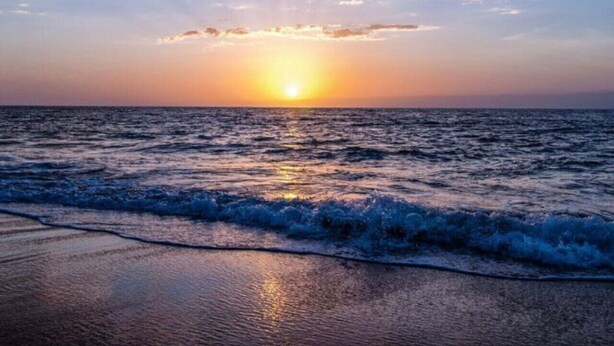 Une plage avec des vagues au coucher du soleil.