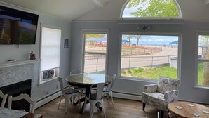 Un coin repas avec une table ronde et des chaises, un ventilateur de plafond et de grandes fenêtres donnant sur l’extérieur.