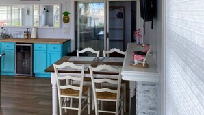 Une cuisine spacieuse avec des meubles de couleur turquoise, une table à manger en bois et des chaises blanches, ainsi qu’une grande fenêtre.
