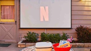 Un écran de projection sur lequel est affiché un grand « N », un bol rouge rempli de collations et une petite table placée devant un bâtiment à la façade en bois.
