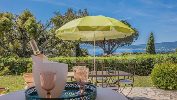 A table with a bottle and glasses, an umbrella, and a view of the sea and hills. - Villa with pool and sea view in Grimaud (GRIMAUD)