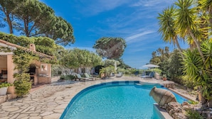 A swimming pool with lounge chairs, surrounded by trees and a stone patio. - Villa with pool and sea view in Grimaud (GRIMAUD)