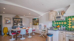 A dining area with a table and chairs, a kitchen with a tiled backsplash, and a trash bin. - Villa with pool and sea view in Grimaud (GRIMAUD)