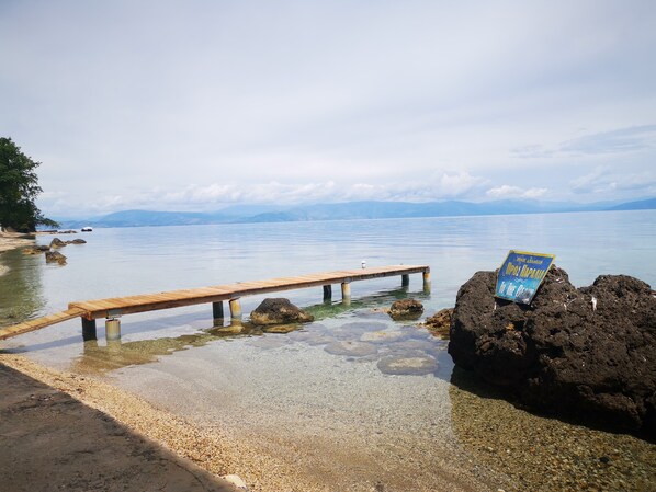 A wooden pier extending into calm waters with a sign on a rock.