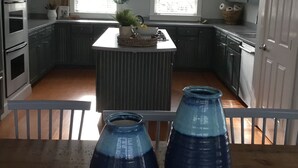 Una cocina con isla central, armarios oscuros y una mesa de comedor de madera con dos jarrones azules.
