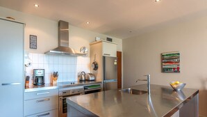 A modern kitchen with stainless steel appliances, a built-in oven, and a large island with a sink. - The Sands - Apartment 23 - Onetangi Beach (Waiheke Island)