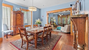 A dining area with a wooden table, chairs, and a chandelier. There is a large wooden cabinet and a window with curtains. - The Laurel Oak Inn Bed and Breakfast (Gainesville)