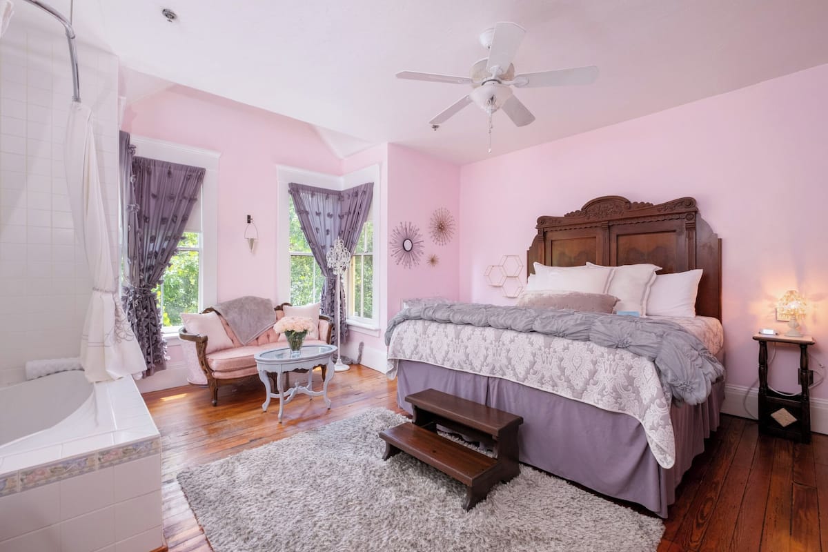 A bedroom with a large bed, a vanity, a chair, and a small table.