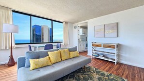 Een moderne woonkamer met een grijze bank, gele kussens, een eettafel en uitzicht op hoge gebouwen.