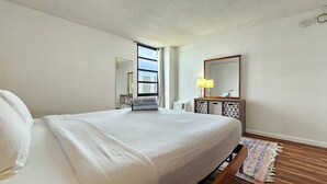 Hotelkamer met een groot bed, nachtkastje met lamp, raam met uitzicht op gebouwen en een kleine spiegel aan de muur.