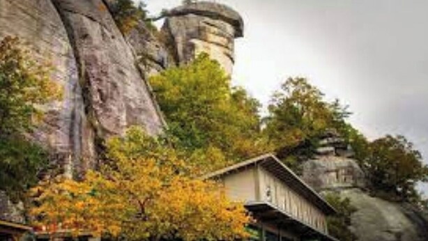 Ein Gebäude im traditionellen Baustil, umgeben von großen Felsformationen und Bäumen mit Herbstlaub.