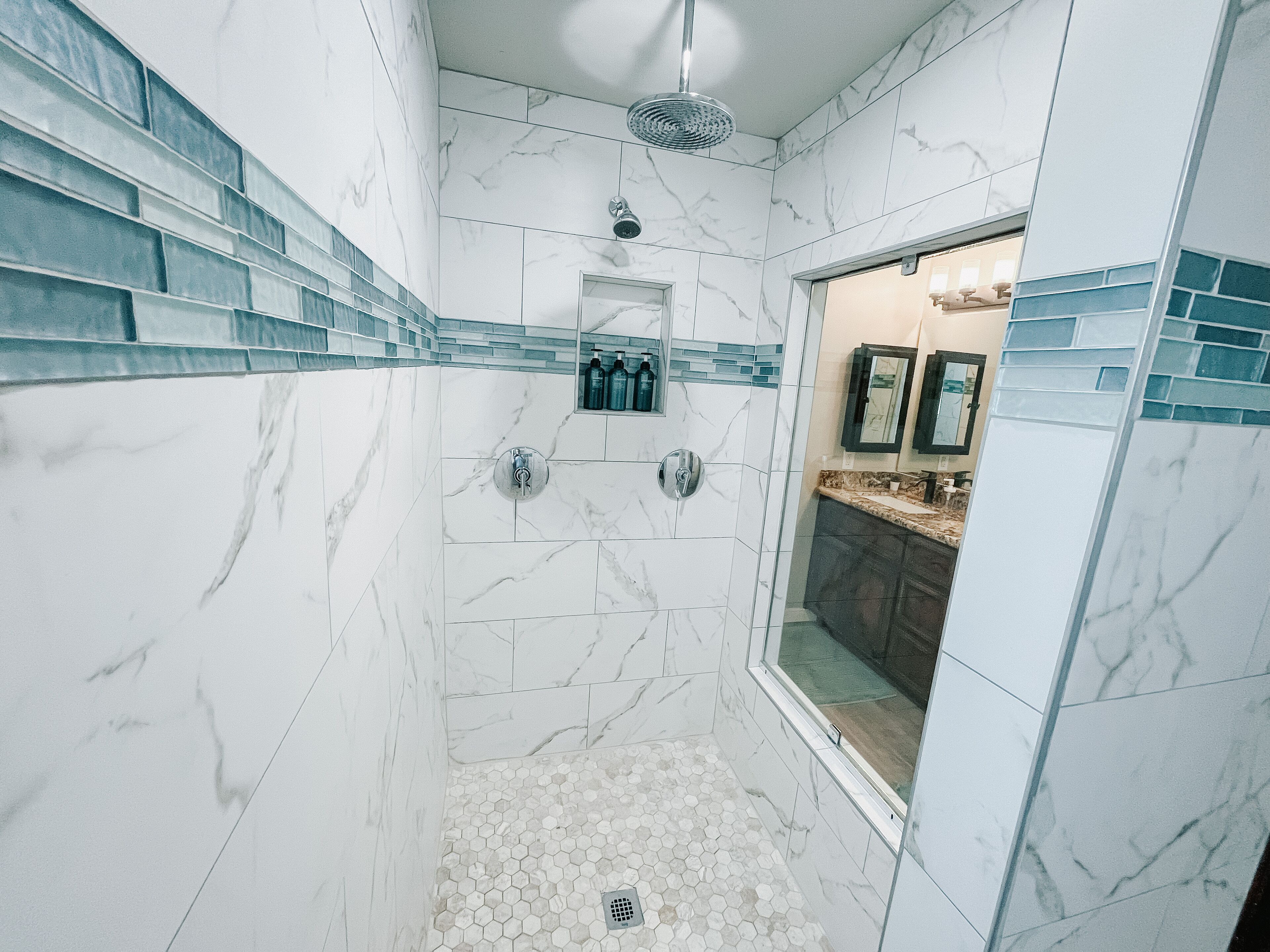 Un baño moderno con paredes de mármol blanco, zona de ducha y tocador con espejo.