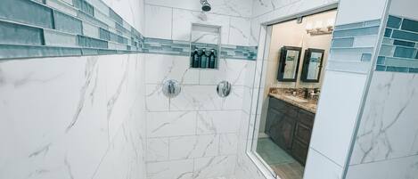 Un baño moderno con paredes de mármol blanco, zona de ducha y tocador con espejo.