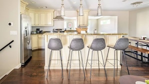 A modern kitchen with a central island, bar stools, stainless steel appliances, and pendant lighting.
