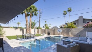 A swimming pool with a sun lounger and a dining area with chairs and a table.