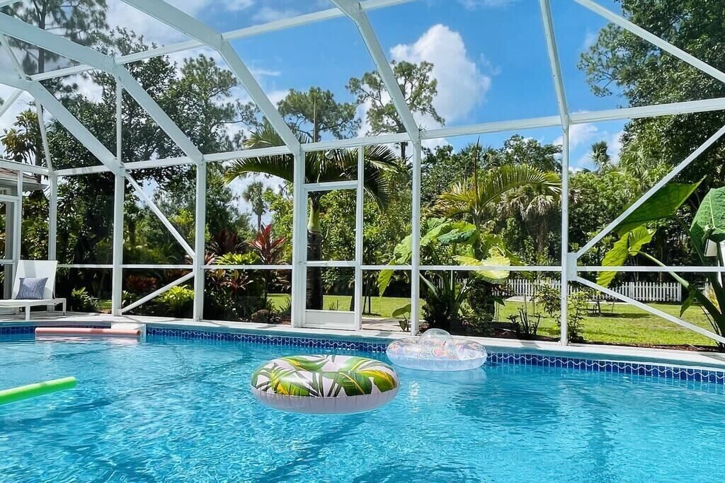 Une piscine intérieure aux parois en verre transparent, entourée d’une végétation luxuriante et d’une clôture blanche.