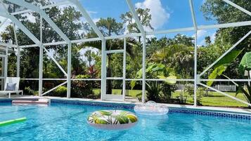 Une piscine intérieure aux parois en verre transparent, entourée d’une végétation luxuriante et d’une clôture blanche.