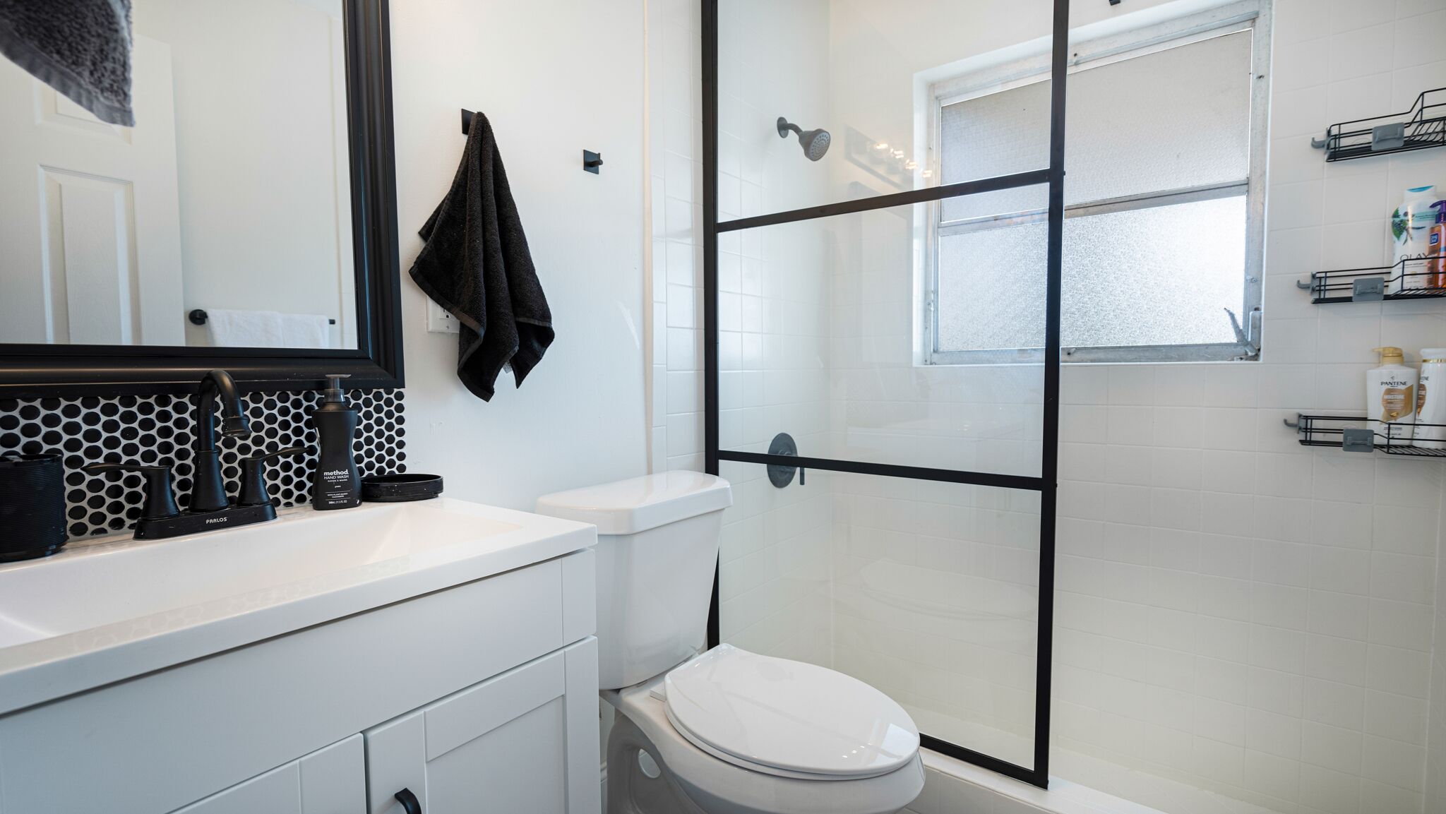 A modern bathroom with a white sink, black towel, and a glass shower enclosure.