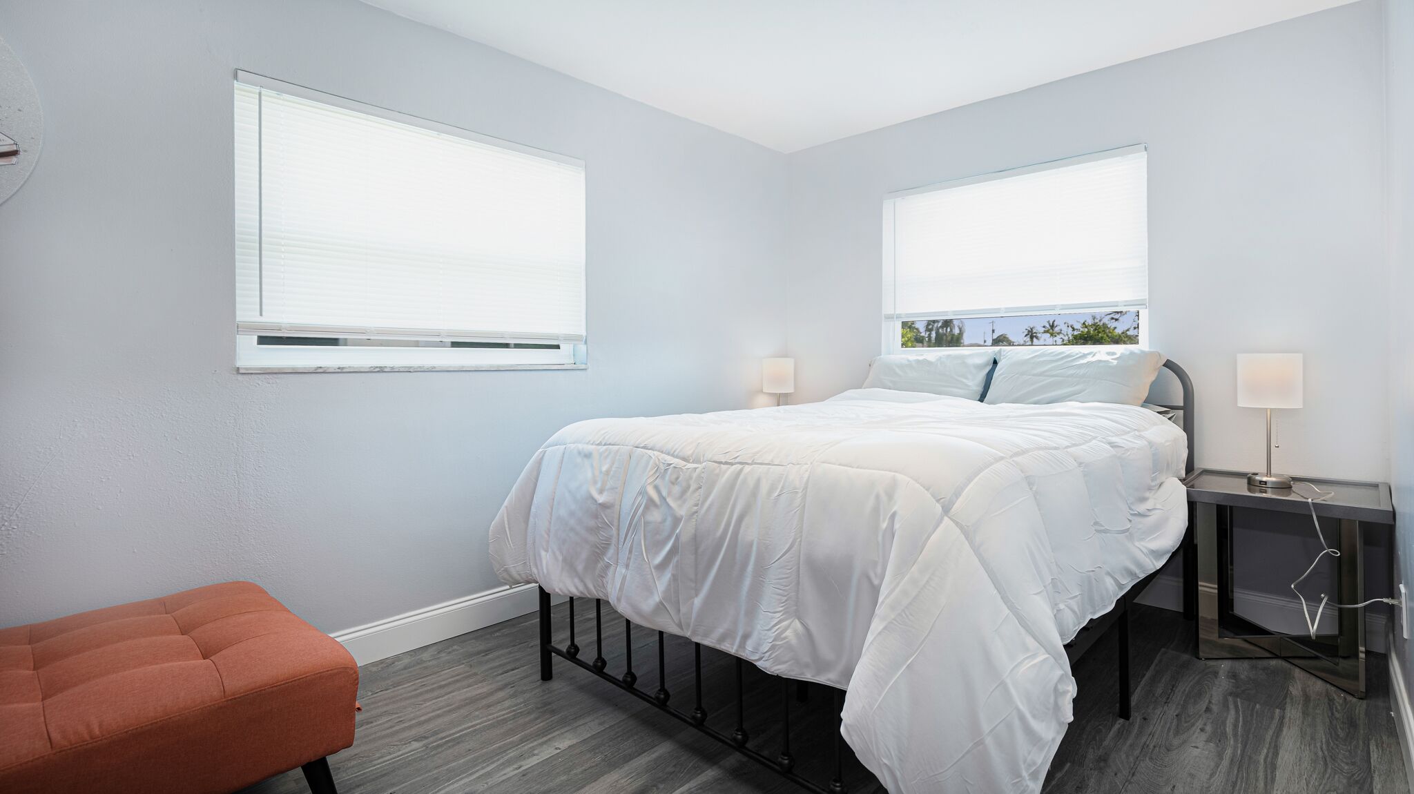 Une chambre moderne comprenant un lit, deux tables de chevet, une commode, une chaise et deux fenêtres.