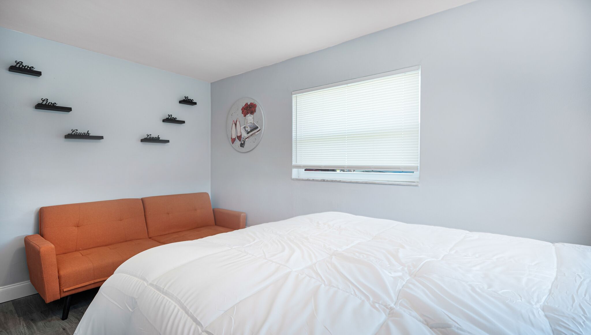 Un dormitorio con cama blanca, sofá naranja y ventana con persianas.