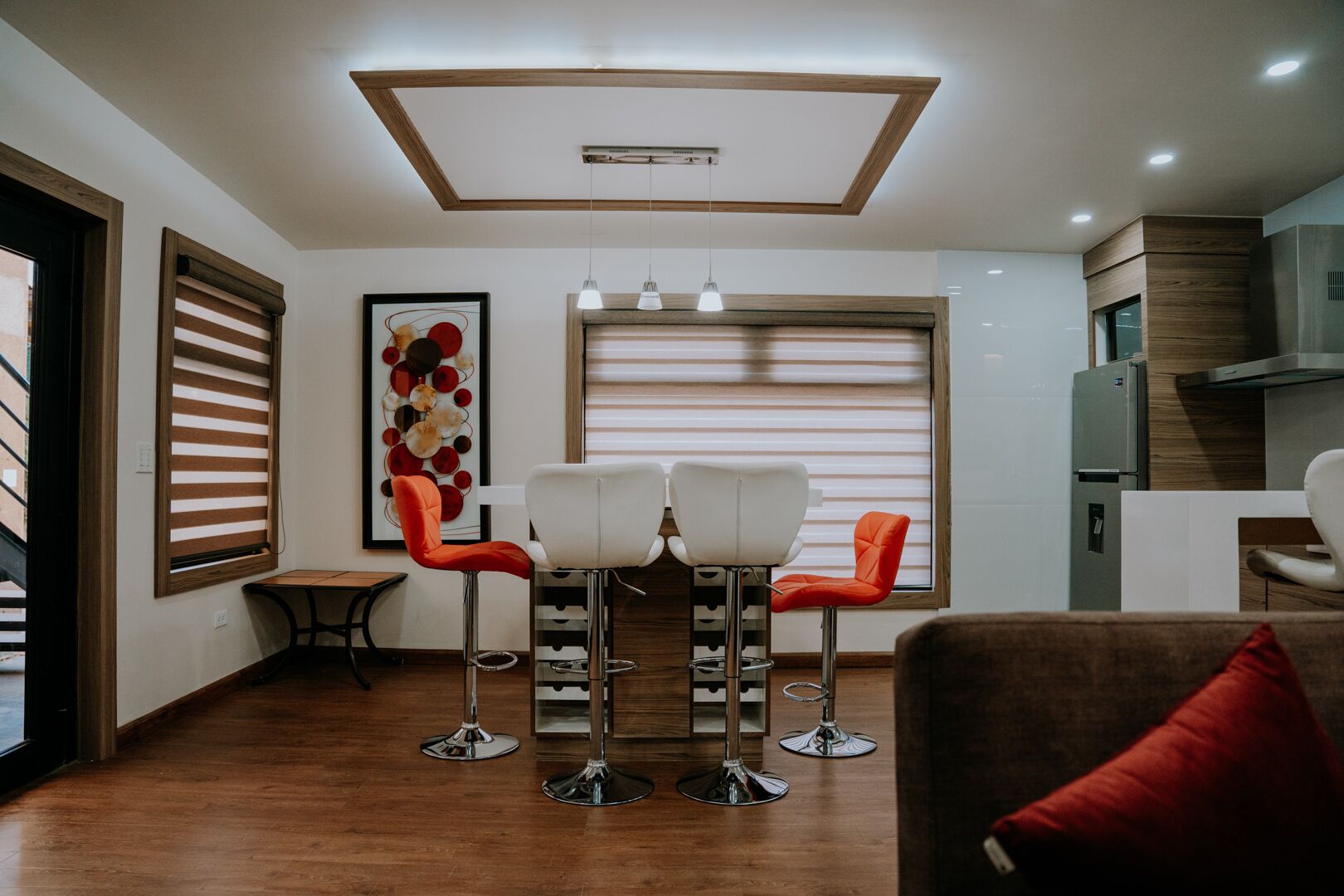 A modern kitchen with a built-in oven, a dining area with two chairs, and a large window with blinds.