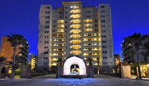Un hôtel de grande hauteur doté de nombreux balcons, d’une arche centrale et de palmiers au premier plan.