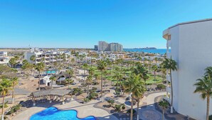 Um resort com piscina, palmeiras e vista para o oceano.