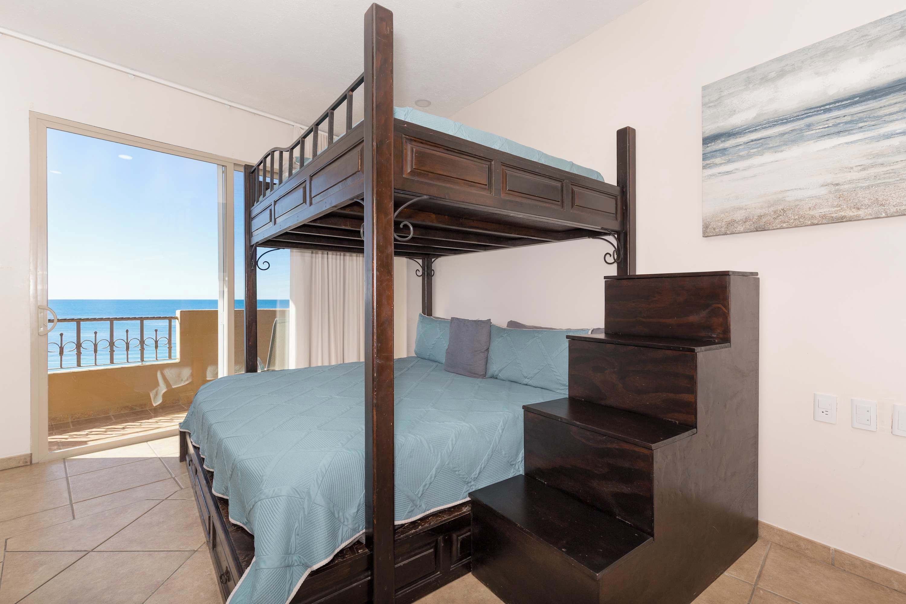 A bedroom with a bunk bed, a balcony with a view of the sea, and a painting on the wall.
