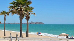 A poolside view with a clear blue sky, palm trees, and a beach in the background. - Fun Sandy Beach Condo B204 at Casa Blanca (Puerto Peñasco)
