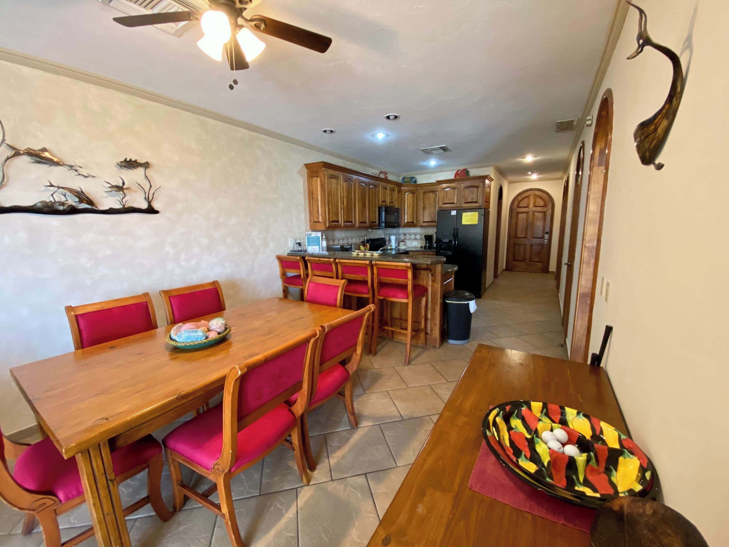 A kitchen with wooden cabinets, a refrigerator, and a dining area with a wooden table and red chairs.