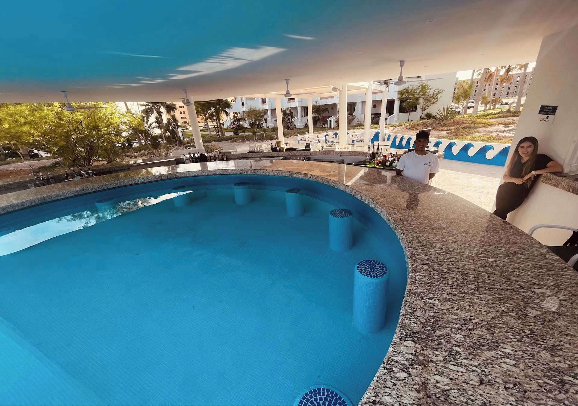 Una piscina de borde curvo, rodeada por una zona techada con suelo de baldosas y encimera de granito.