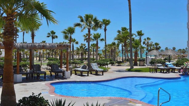 A pool area with lounge chairs, palm trees, and a clear blue sky. - Fun Sandy Beach Condo B204 at Casa Blanca (Puerto Peñasco)