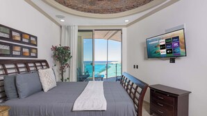Un dormitorio con una cama grande, un televisor montado en la pared y vista al océano a través de una puerta corrediza.