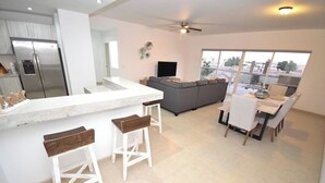Een moderne keuken met een groot eiland, een grijze bank en een eethoek met witte stoelen.