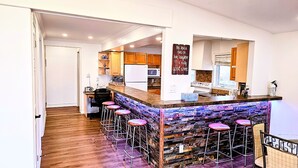 A kitchen with wooden cabinets, a microwave, and a stove. There are bar stools and a bar counter with a decorative backsplash. - Lakeside Dreams: Retreat with Stunning Views, private Beach Access (Bowmanville)