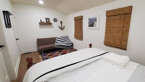 A bedroom with a bed, a sofa, a patterned rug, a wooden floor, and wall decorations including a ship's wheel and a framed picture. - Lakeside Dreams: Retreat with Stunning Views, private Beach Access (Bowmanville)