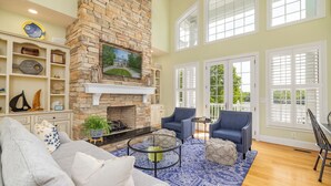 A spacious living room with a stone fireplace, comfortable seating, and large windows. - Blue Heaven (Littleton)