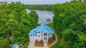A large white house with a blue roof, surrounded by lush green trees and a lake. - Blue Heaven (Littleton)