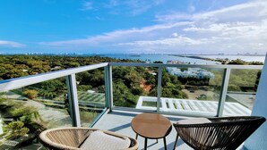 A balcony with a glass railing, two wicker chairs, and a small table. - Design District Bay View Cielo Stays (Miami)