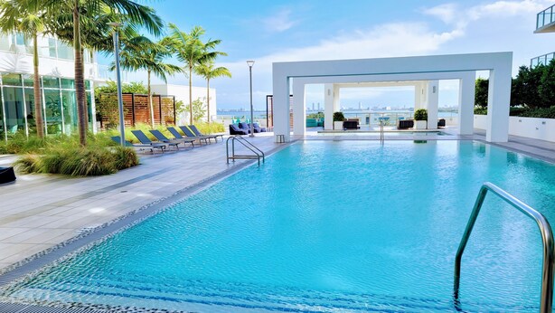 A modern pool area with clear blue water, sun loungers, and a view of the city skyline. - Design District Bay View Cielo Stays (Miami)