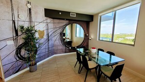 A dining area with a glass table, black chairs, a potted plant, and a large window with a view. - Design District Bay View Cielo Stays (Miami)