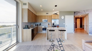 Enjoy cooking in this kitchen with a sleek island, microwave, and stainless steel refrigerator, offering a view of the city.
