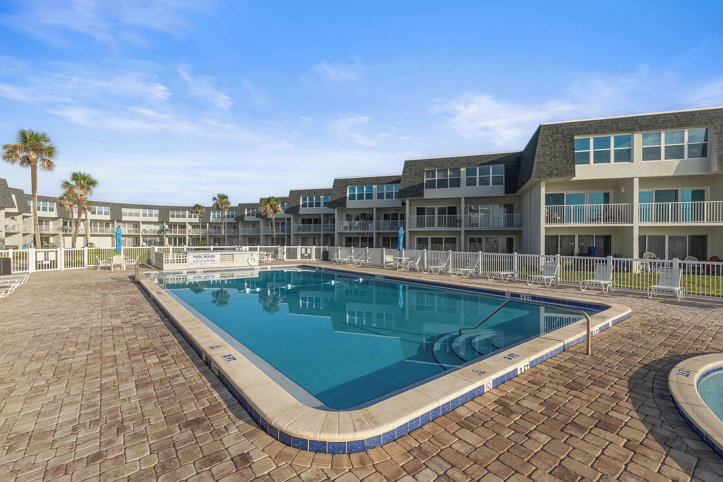 A rectangular swimming pool with a tiled edge, surrounded by a brick patio.