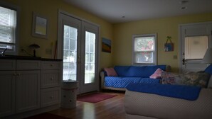 A living room with a sofa, a kitchen area, and a door with a window. - LYC Cottage #1 (Port Austin)