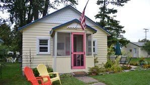 A small house with a pink door and windows, a small porch, and two Adirondack chairs. - LYC Cottage #1 (Port Austin)